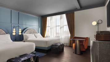 A hotel room with two beds, a small table, a chair, and a desk with a radio.