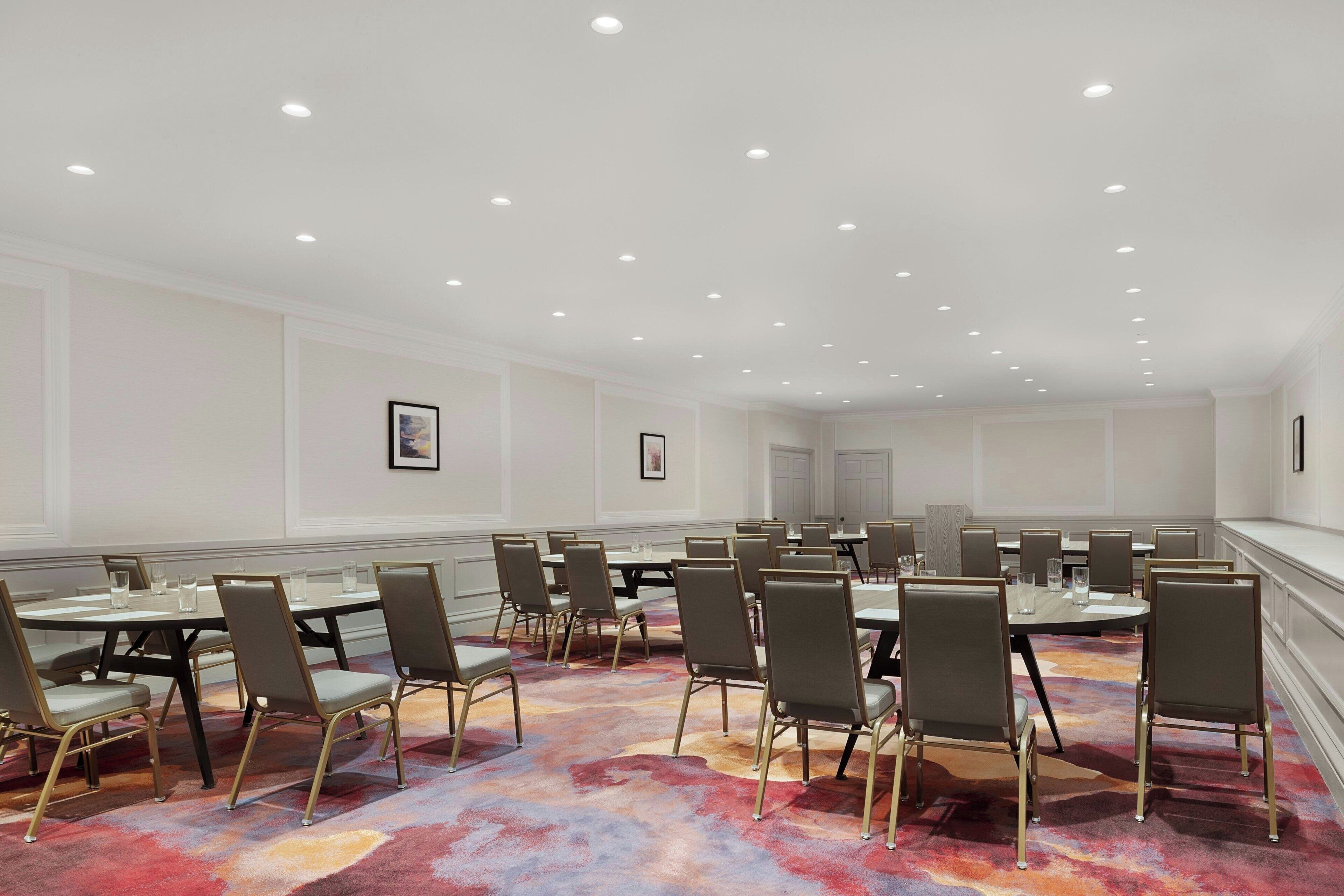 A conference room with round tables and chairs, white walls, and recessed ceiling lights.