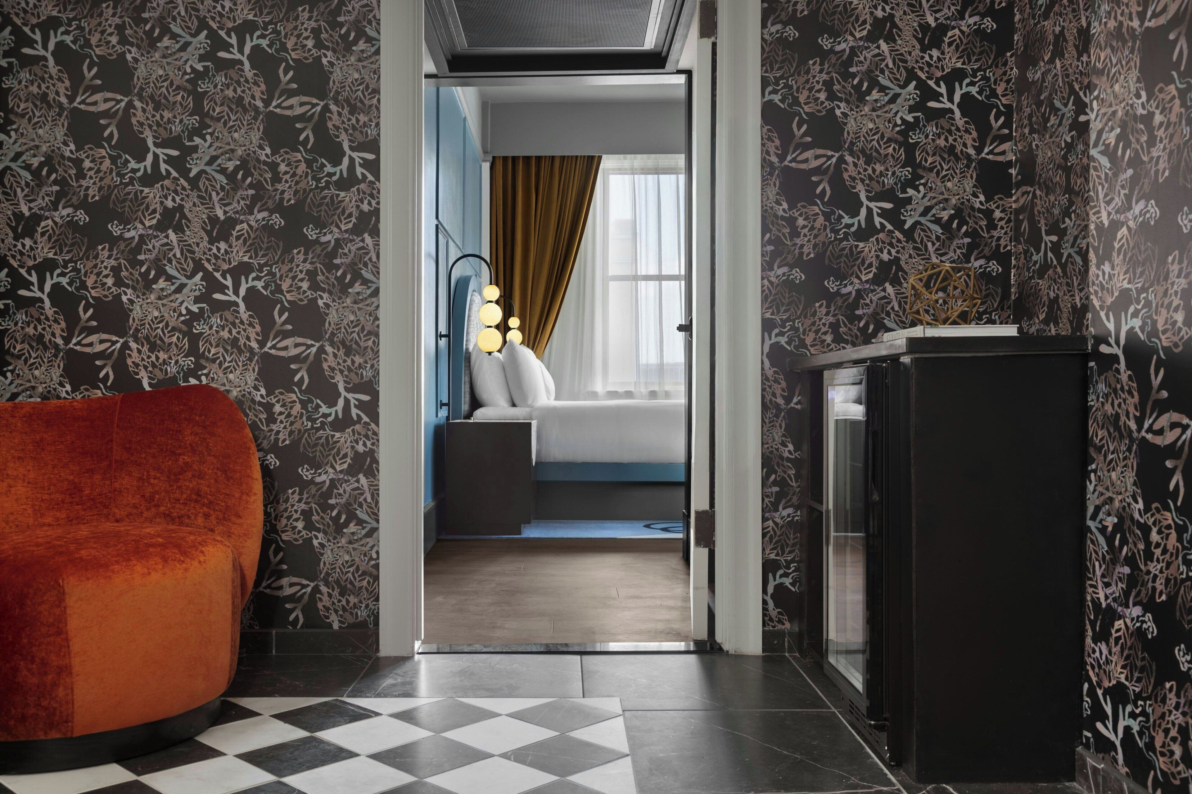 A hotel room with a checkered floor, a bed, a nightstand, a desk, and a chair.