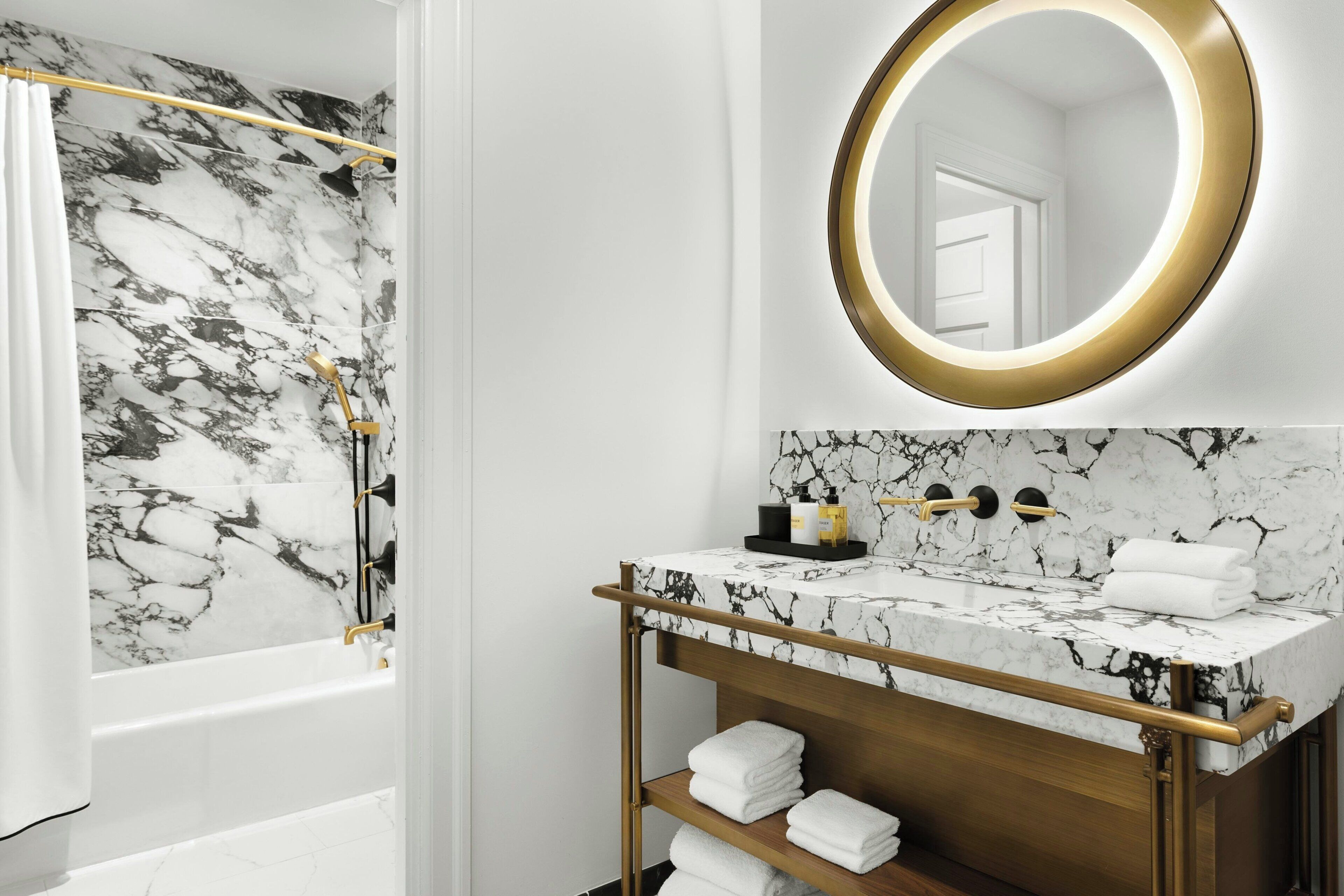 A bathroom with a marble vanity, a gold-framed mirror, and a shower with a marble wall.