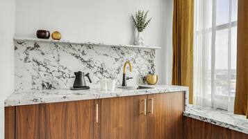 A kitchen with marble backsplash, wooden cabinets, and a window with curtains.