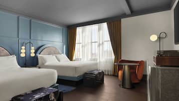 Habitación de hotel con dos camas, un escritorio, una silla, un aparador y un ventanal con cortinas.