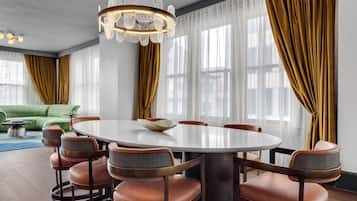 A dining area with a round table, six chairs, and a chandelier. There is a green sofa in the background.