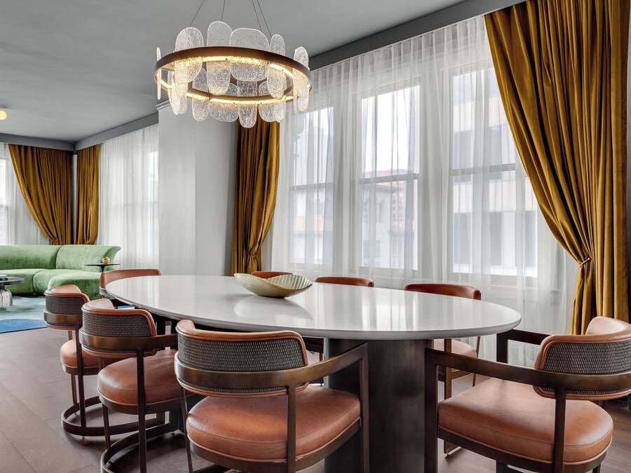 A dining area with a round table, six chairs, and a chandelier. There is a green sofa in the background.