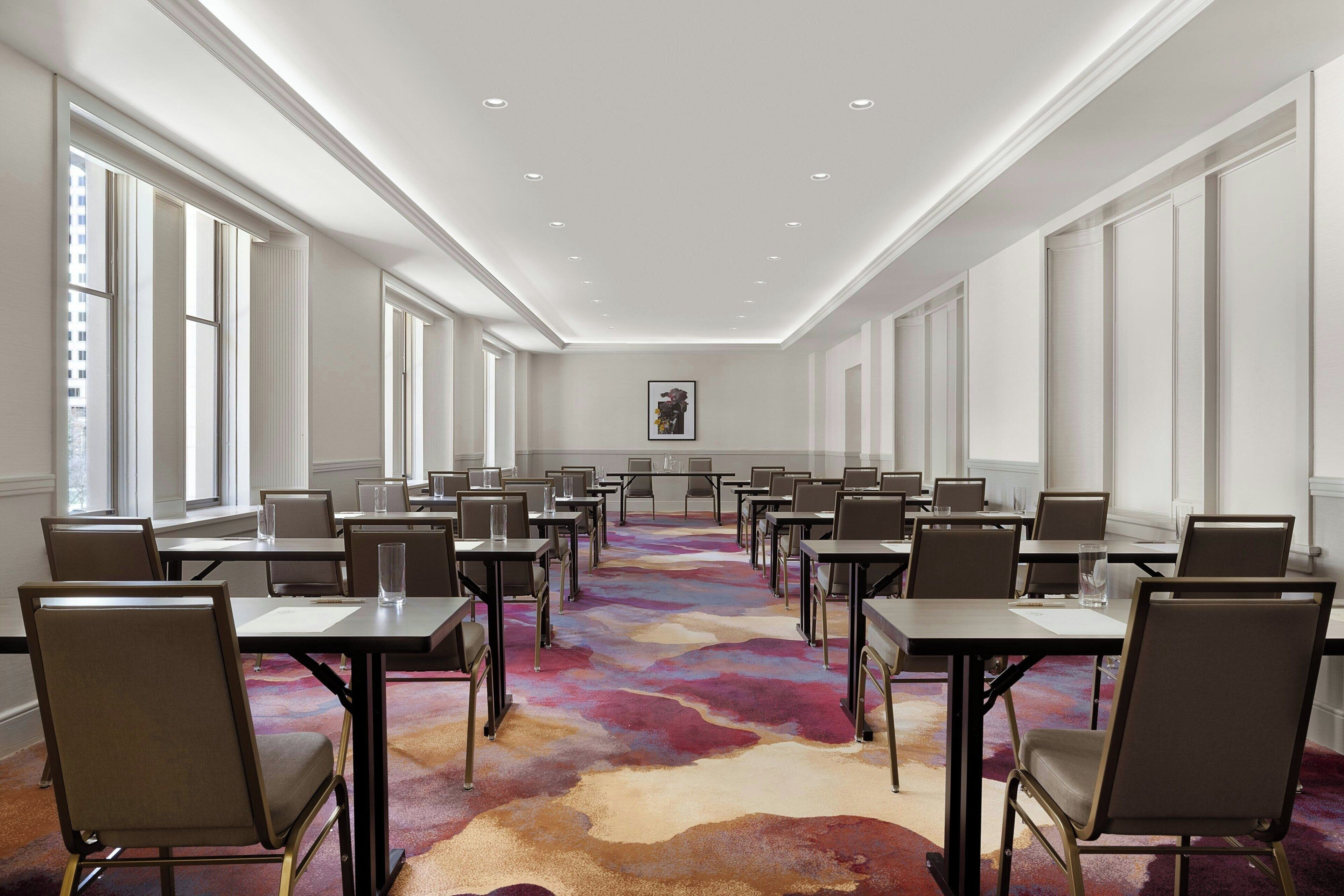 A conference room with multiple tables and chairs, large windows, and a colorful carpet.