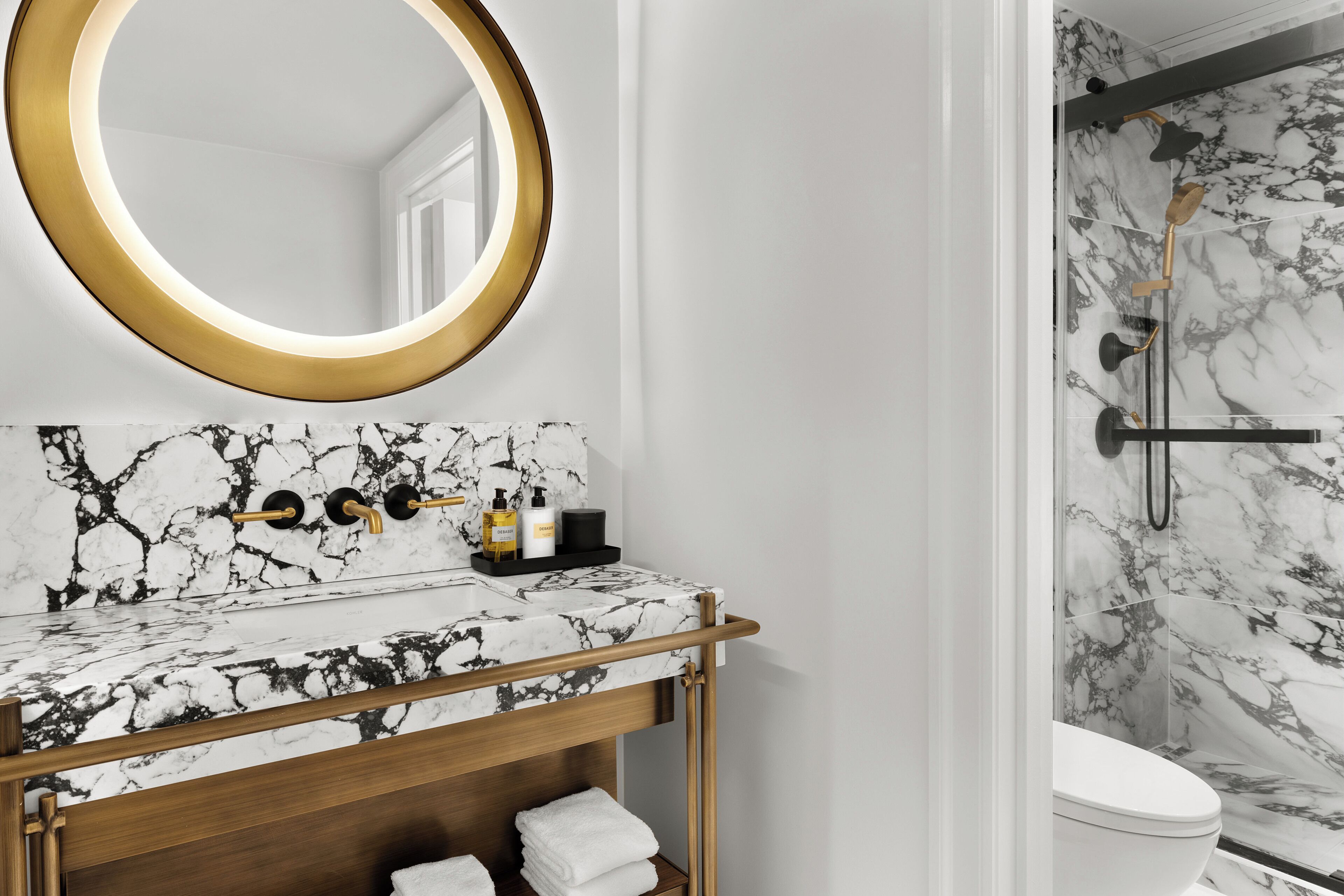 A bathroom with a marble vanity, a gold-framed mirror, and a shower with marble walls.