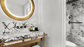A bathroom with a marble vanity, a round mirror with a gold frame, and a shower with a marble wall.