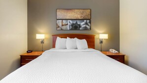 Une chambre d’hôtel avec un grand lit, deux tables de chevet avec des lampes, une tête de lit en bois et des œuvres d’art abstraites accrochées au mur.