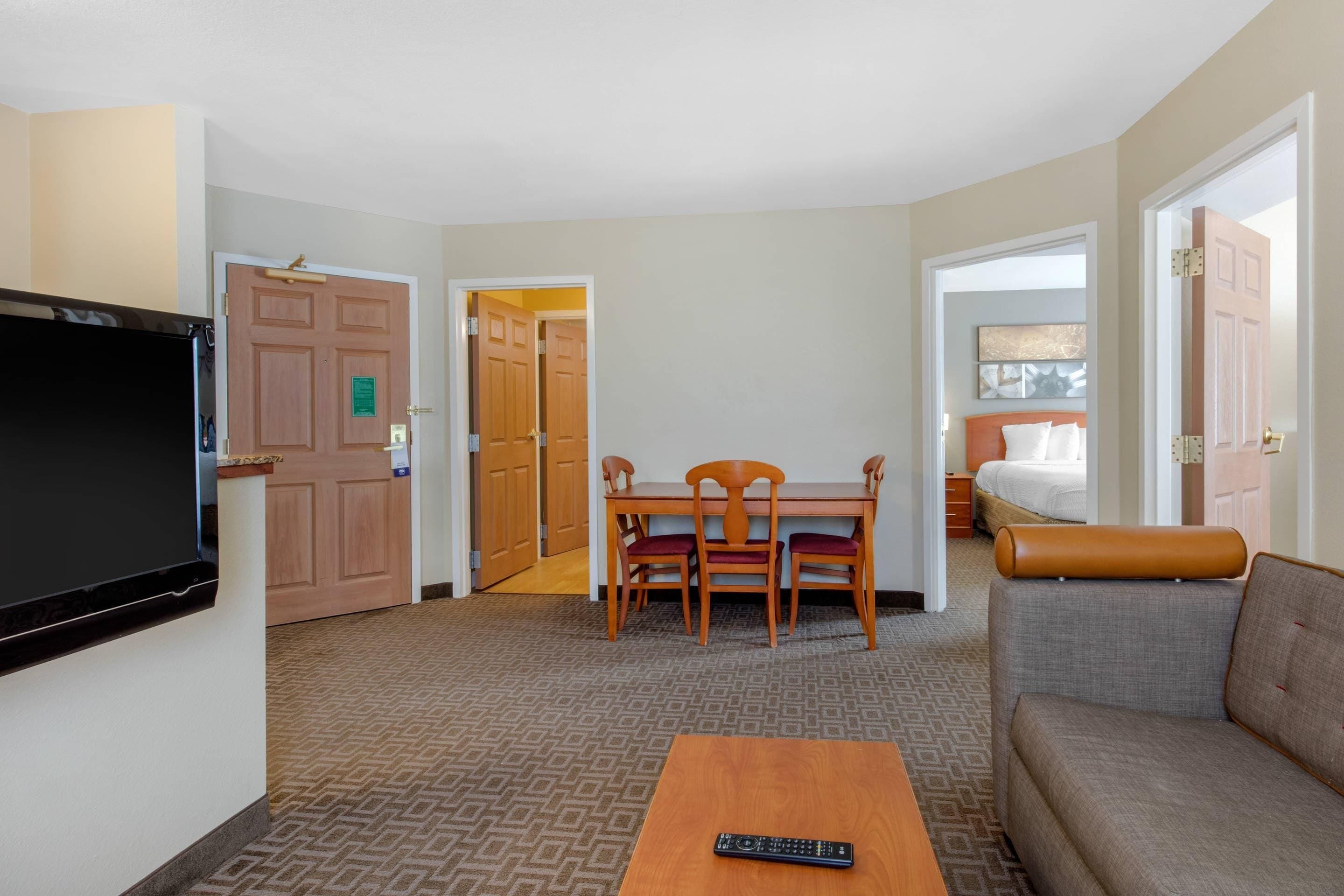 Una habitación de hotel con televisión, una mesa de comedor con sillas, un sofá y una cama.