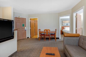 A hotel room with a television, a dining table with chairs, a sofa, and a bed.