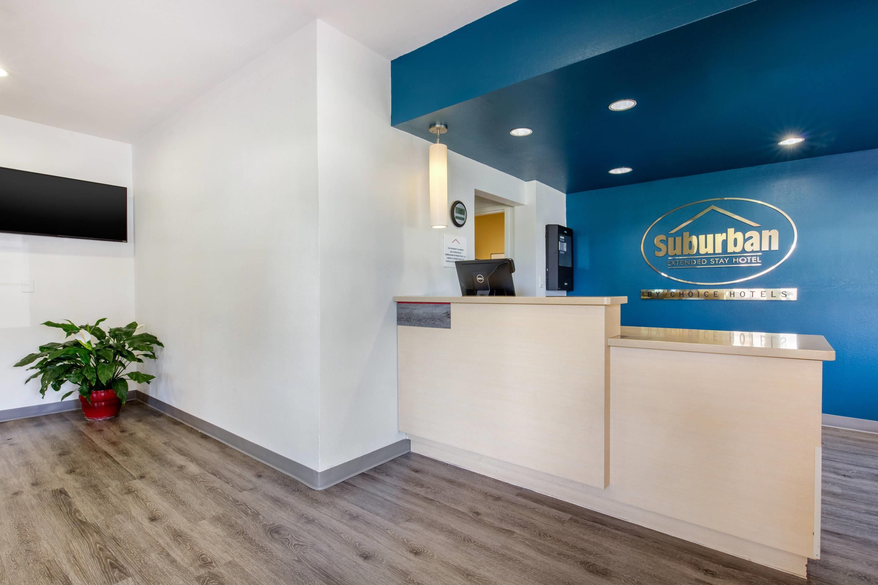 Un comptoir d’accueil avec un mur bleu et une enseigne indiquant « Suburban Extended Stay Hotel ».