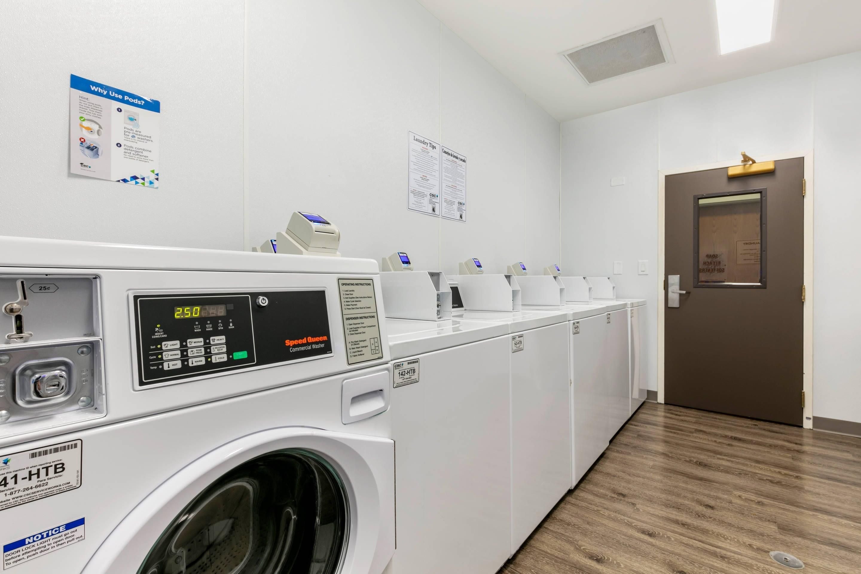 A laundry facility with multiple washing machines, a control panel, and informational posters on the walls.