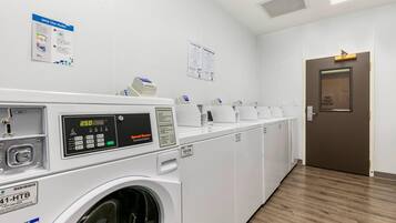 A laundry facility with multiple washing machines, a control panel, and informational posters on the walls.
