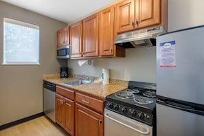 Una cocina con armarios de madera, un refrigerador de acero inoxidable, una estufa y un microondas.