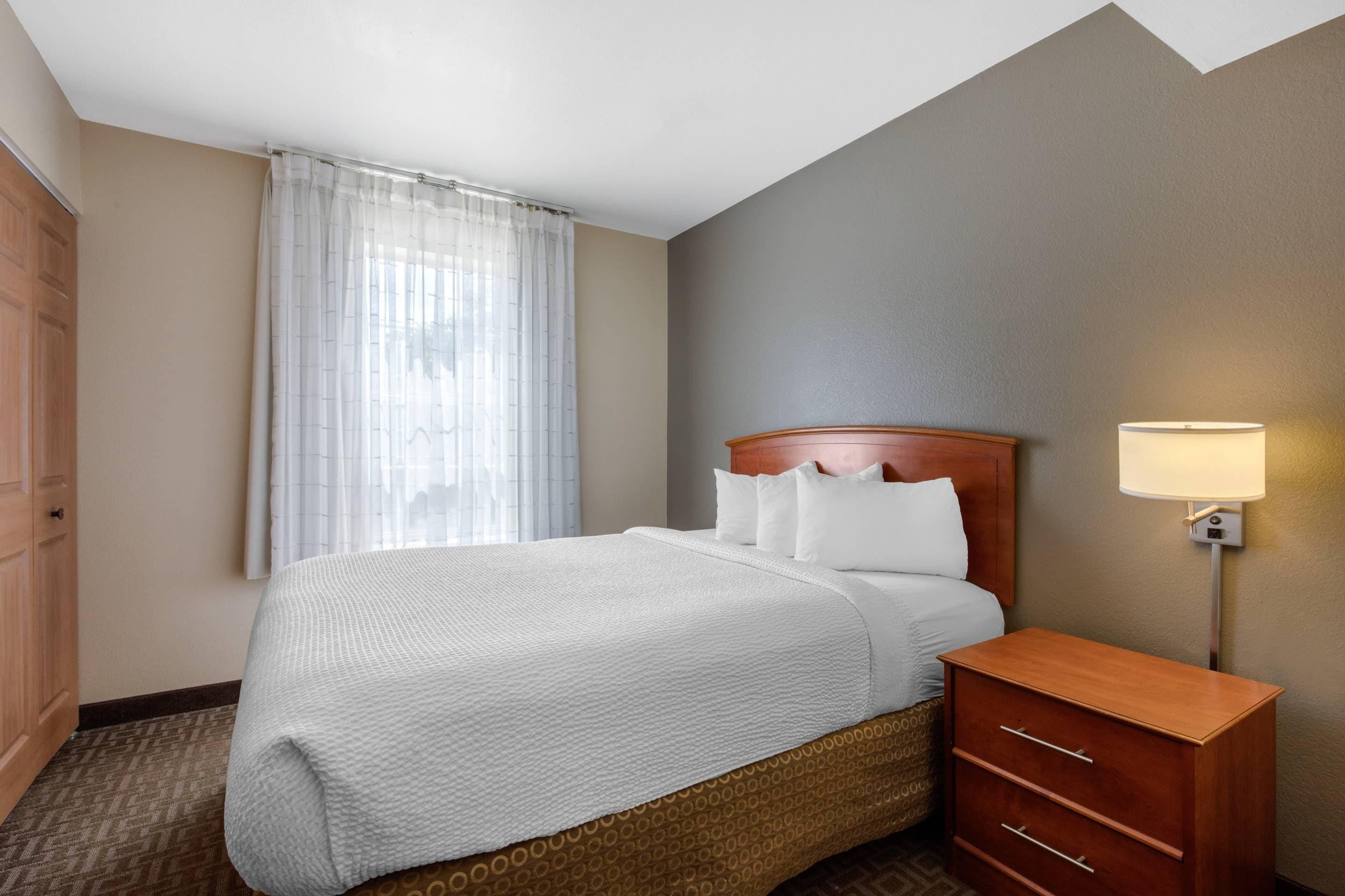 A hotel room with a bed, a nightstand, a lamp, and a window with curtains.
