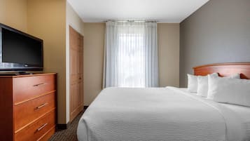 Una habitación de hotel con una cama, un televisor en una cómoda, un armario y una ventana con cortinas.