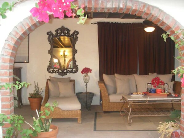 A cozy living room with a brick archway, a sofa, a chair, a table, and potted plants. - Tuscan Springs Hotel & Spa (Desert Hot Springs)