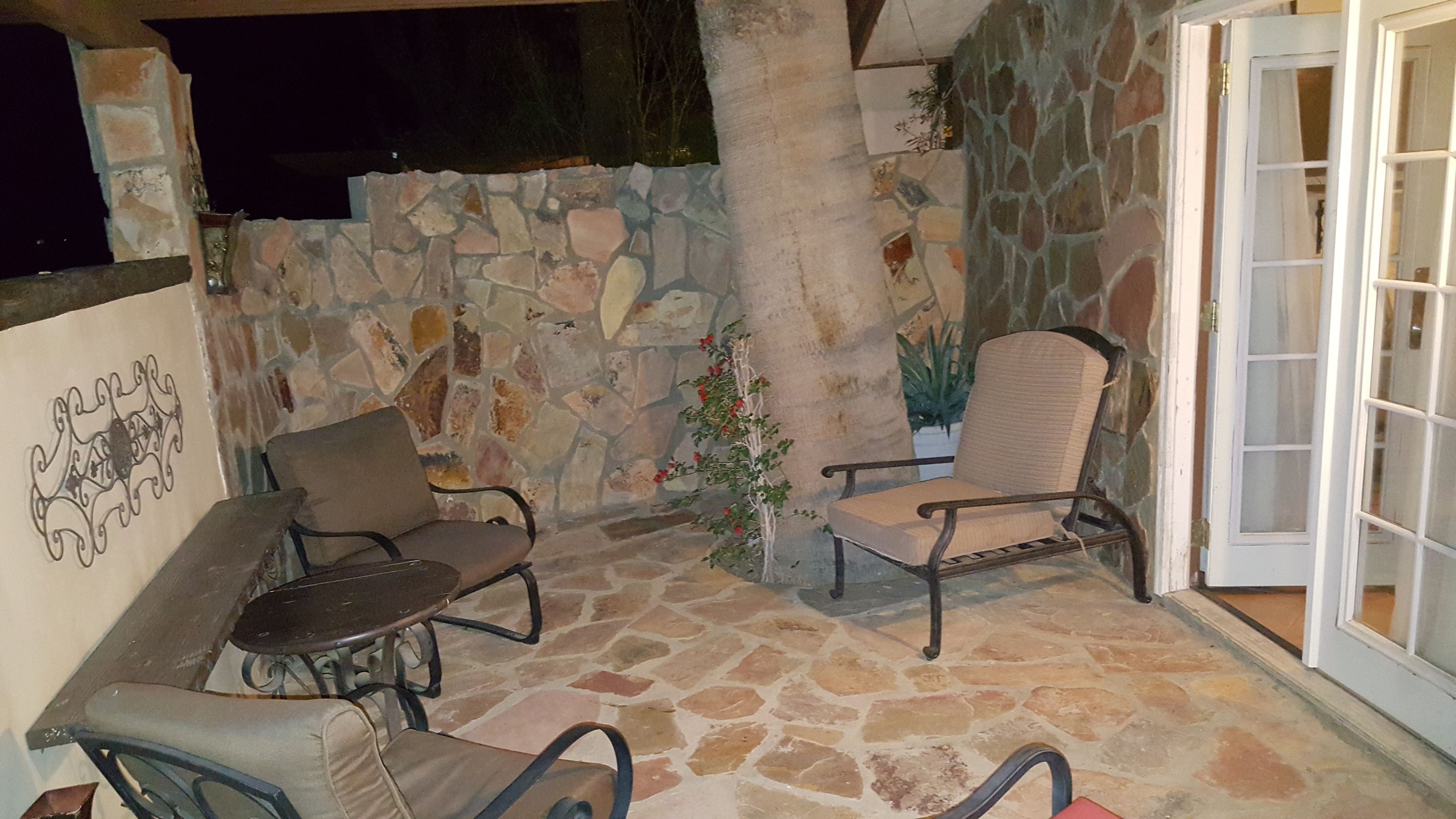 Une terrasse extérieure avec un sol en pierre, deux chaises, une table et un mur en pierre.
