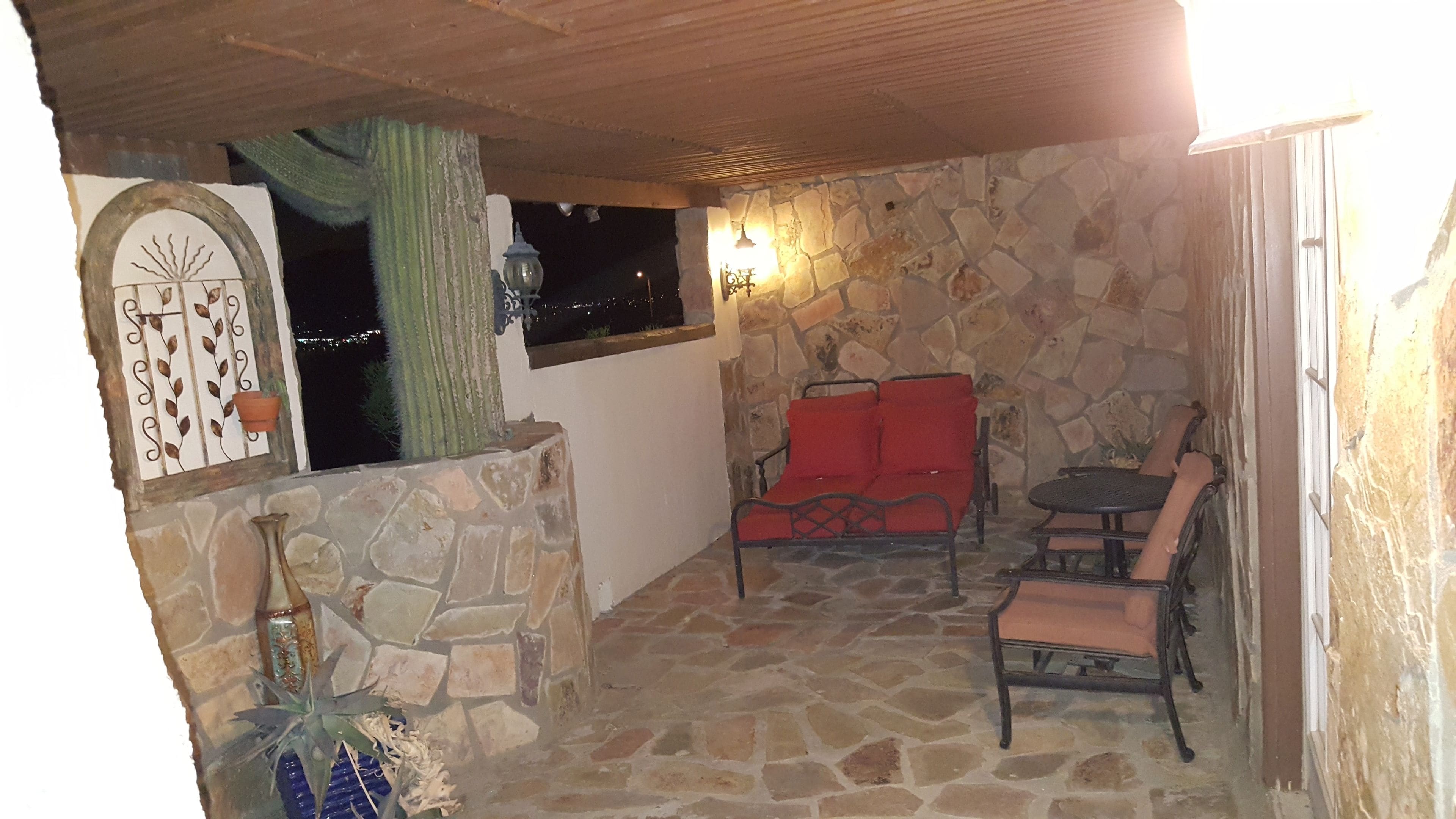 Une terrasse dallée de pierre avec un coin salon doté de coussins rouges, une petite table et un mur décoratif agrémenté d’une fenêtre.