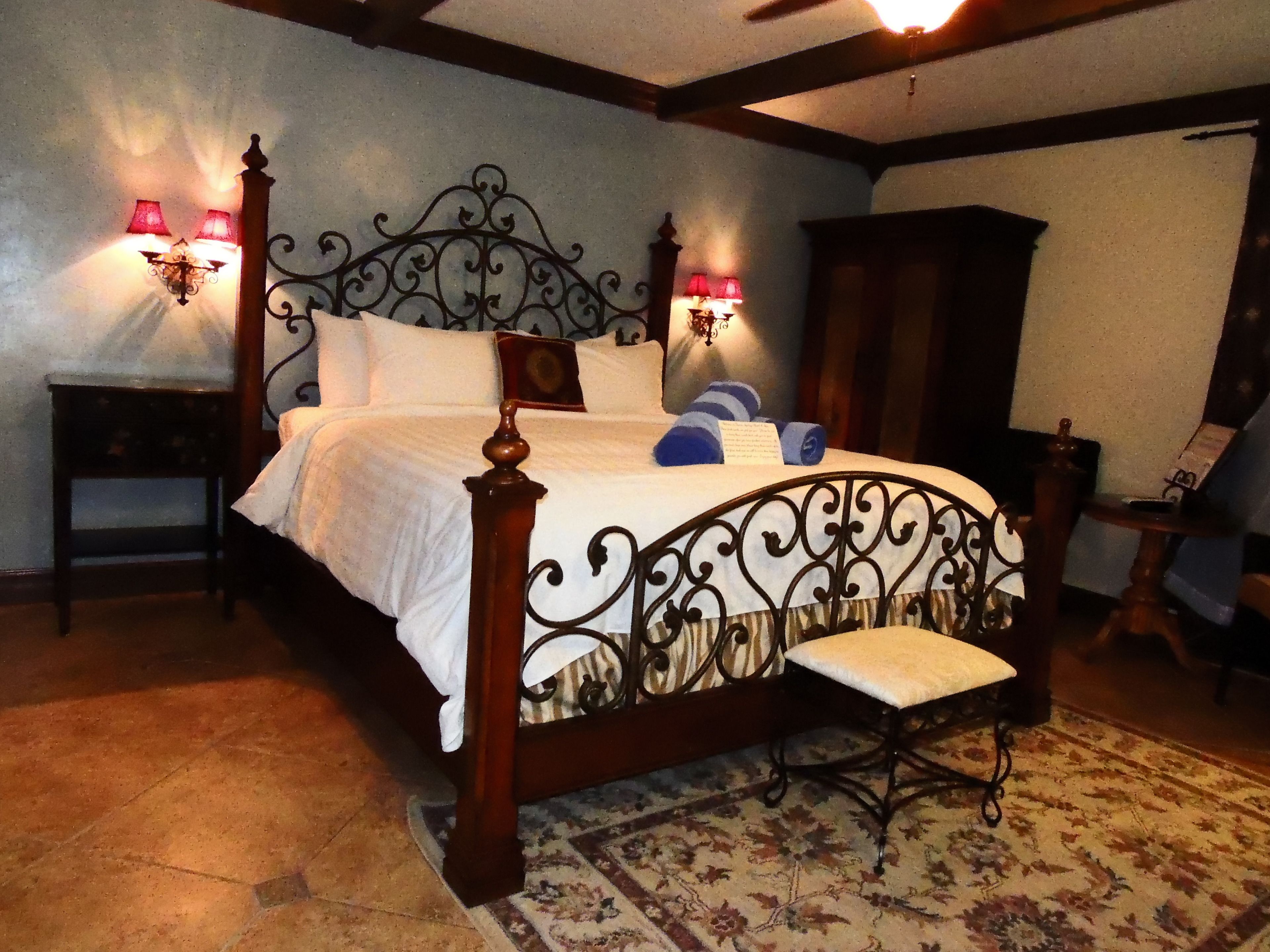 A bedroom with a four-poster bed, two bedside tables with lamps, a chair, and a patterned rug.