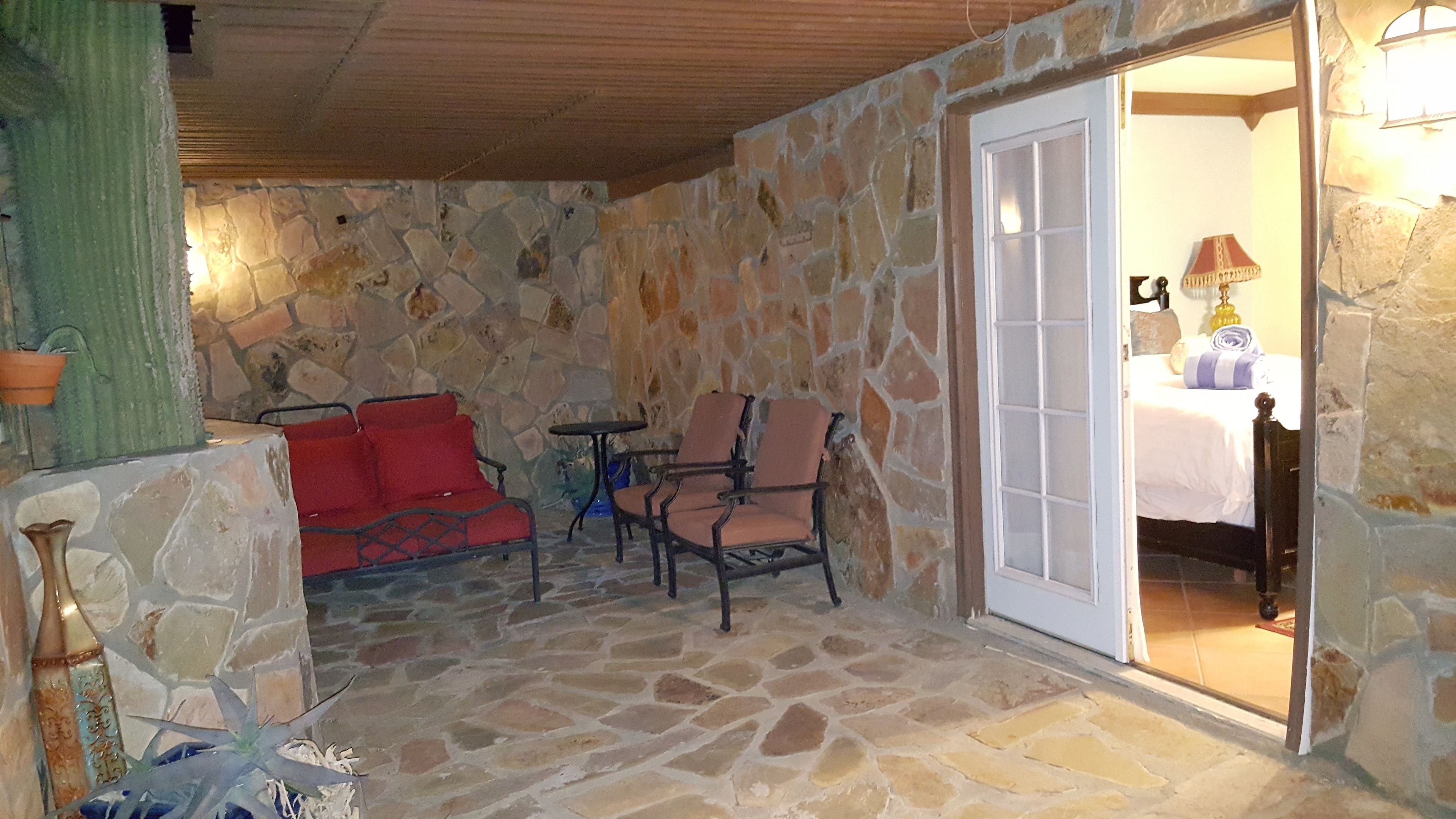 A stone-floored patio with a red sofa, two armchairs, and a small table.