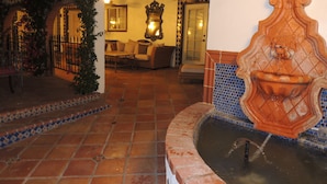 Un patio con una fuente, suelo de baldosas y una zona de estar con sofá y mesa.