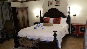 Un dormitorio tradicional con una cama grande, un armario de madera, una mesita pequeña y un aparador decorativo.