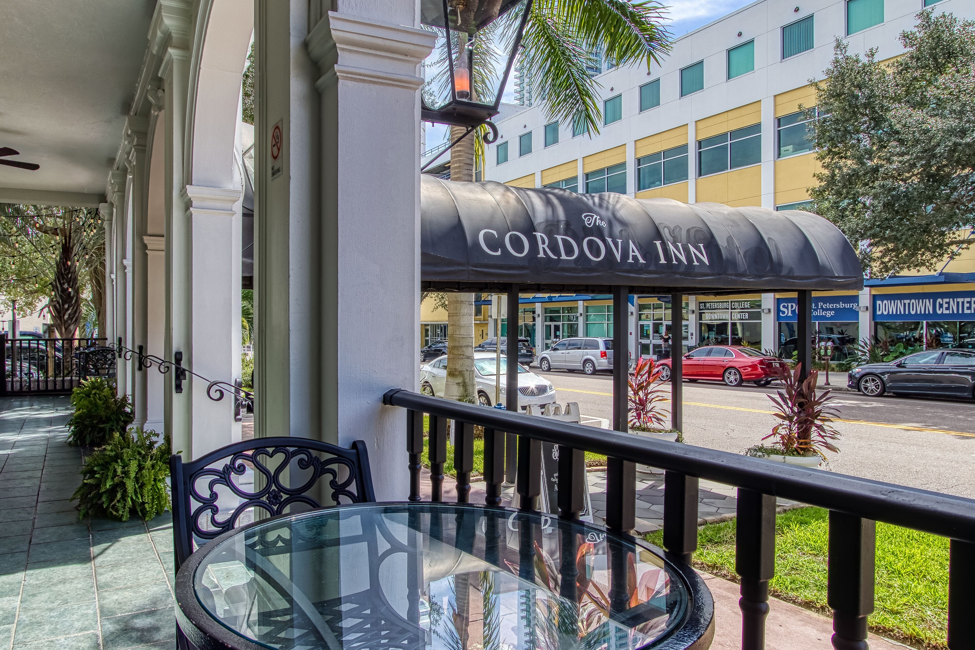 A glass table and chair on a balcony with a view of a building labeled "CORDOVA INN" and a street with cars.