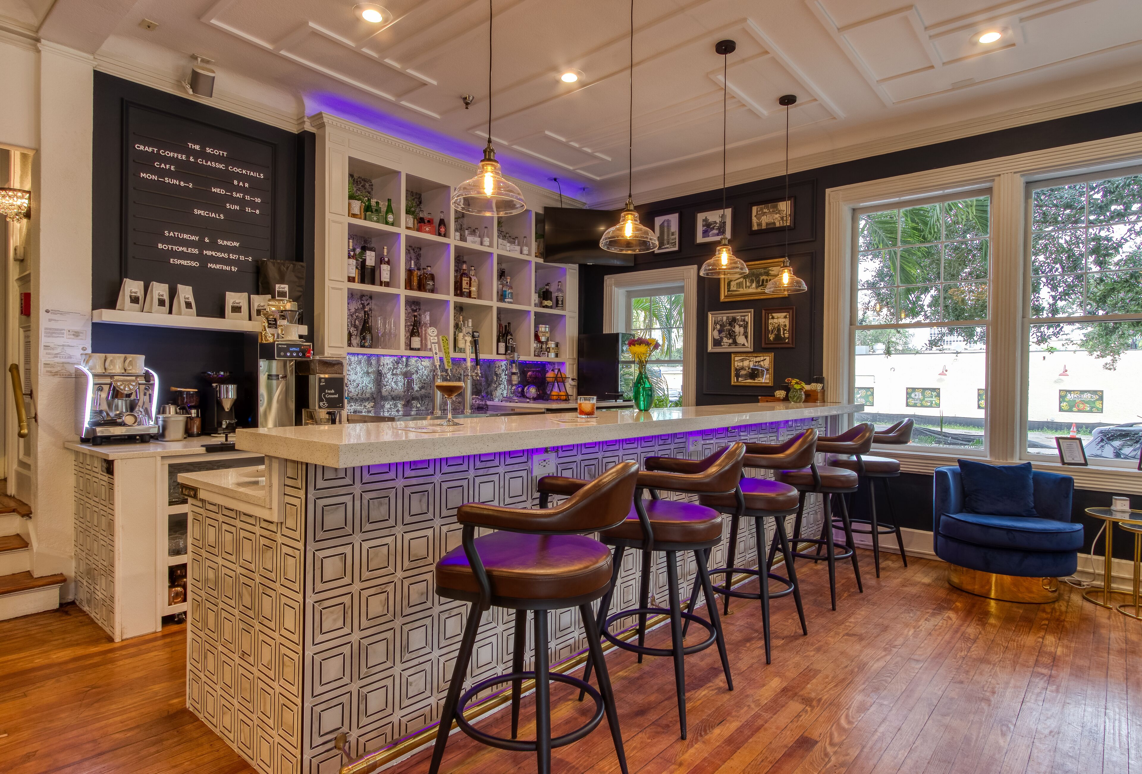 Una zona de bar con barra, taburetes y estantes con botellas.