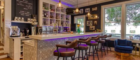 Una zona de bar con barra, taburetes y estantes con botellas.