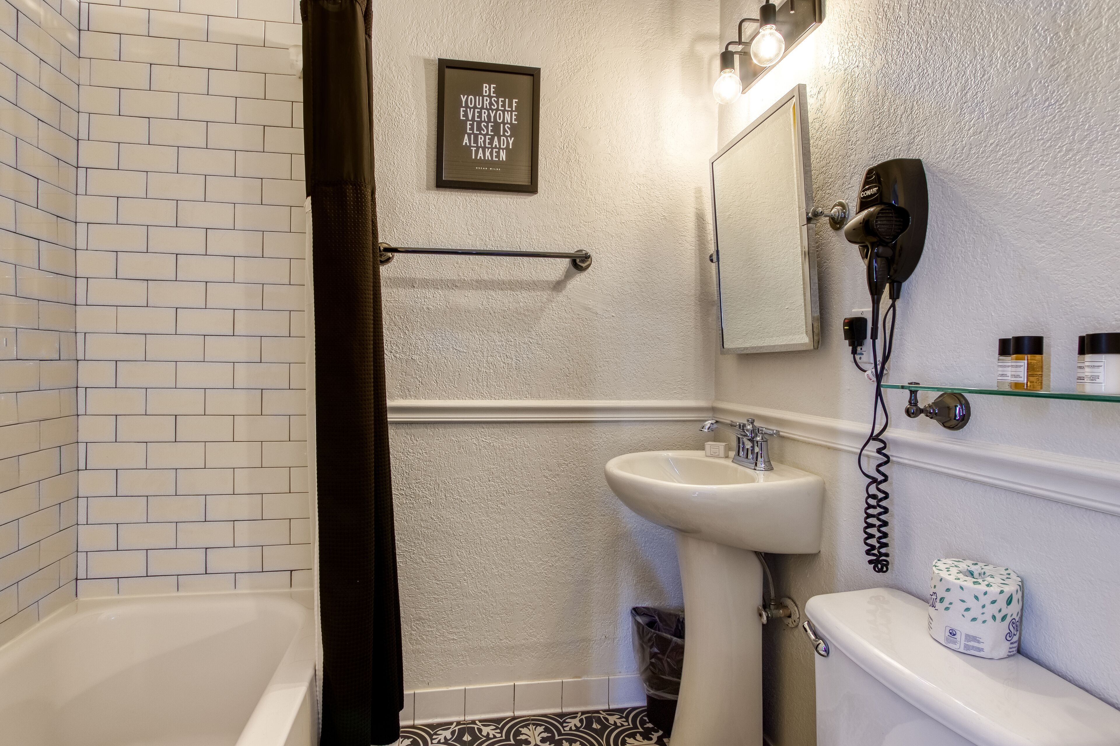 Uma casa de banho com uma banheira branca, um lavatório, um secador de cabelo fixado na parede e uma frase emoldurada na parede.