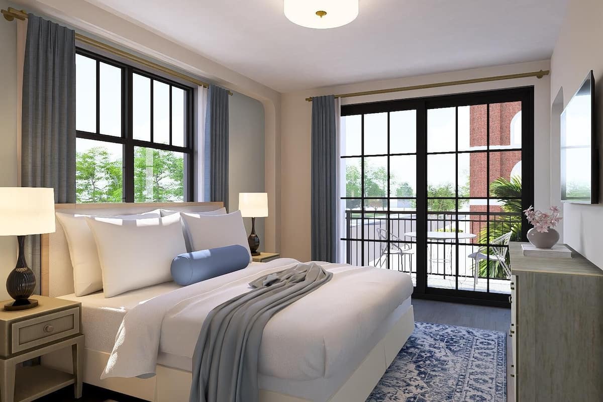 A hotel room with a large bed, two bedside tables with lamps, a view through a sliding glass door to an outdoor area, and a mounted TV on the wall.
