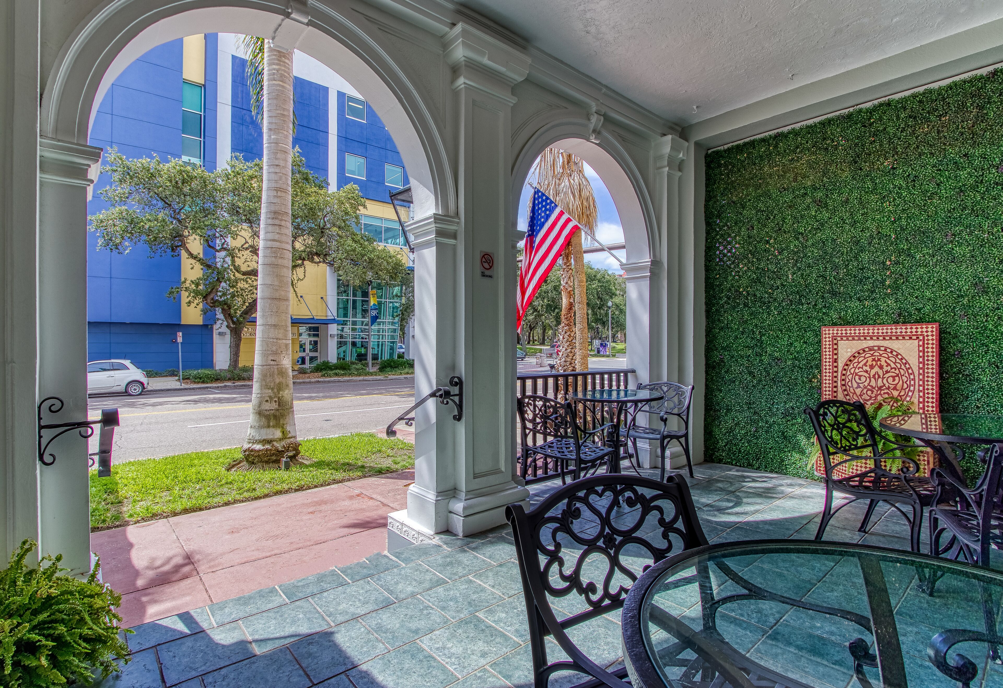Un patio al aire libre con una mesa y sillas de vidrio, una palmera y vistas de un edificio azul.