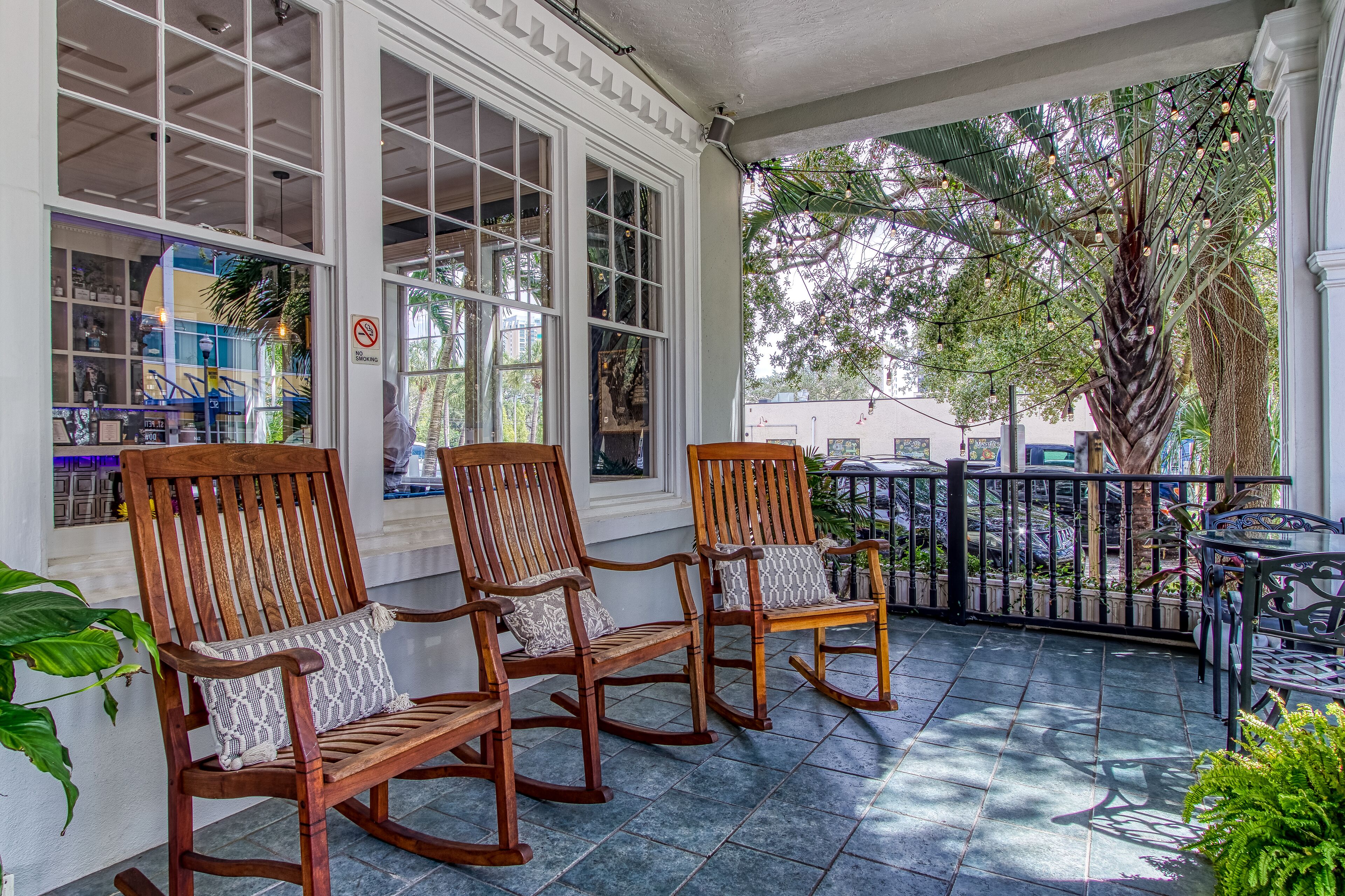 A covered outdoor seating area with wooden rocking chairs and a view of a street scene.