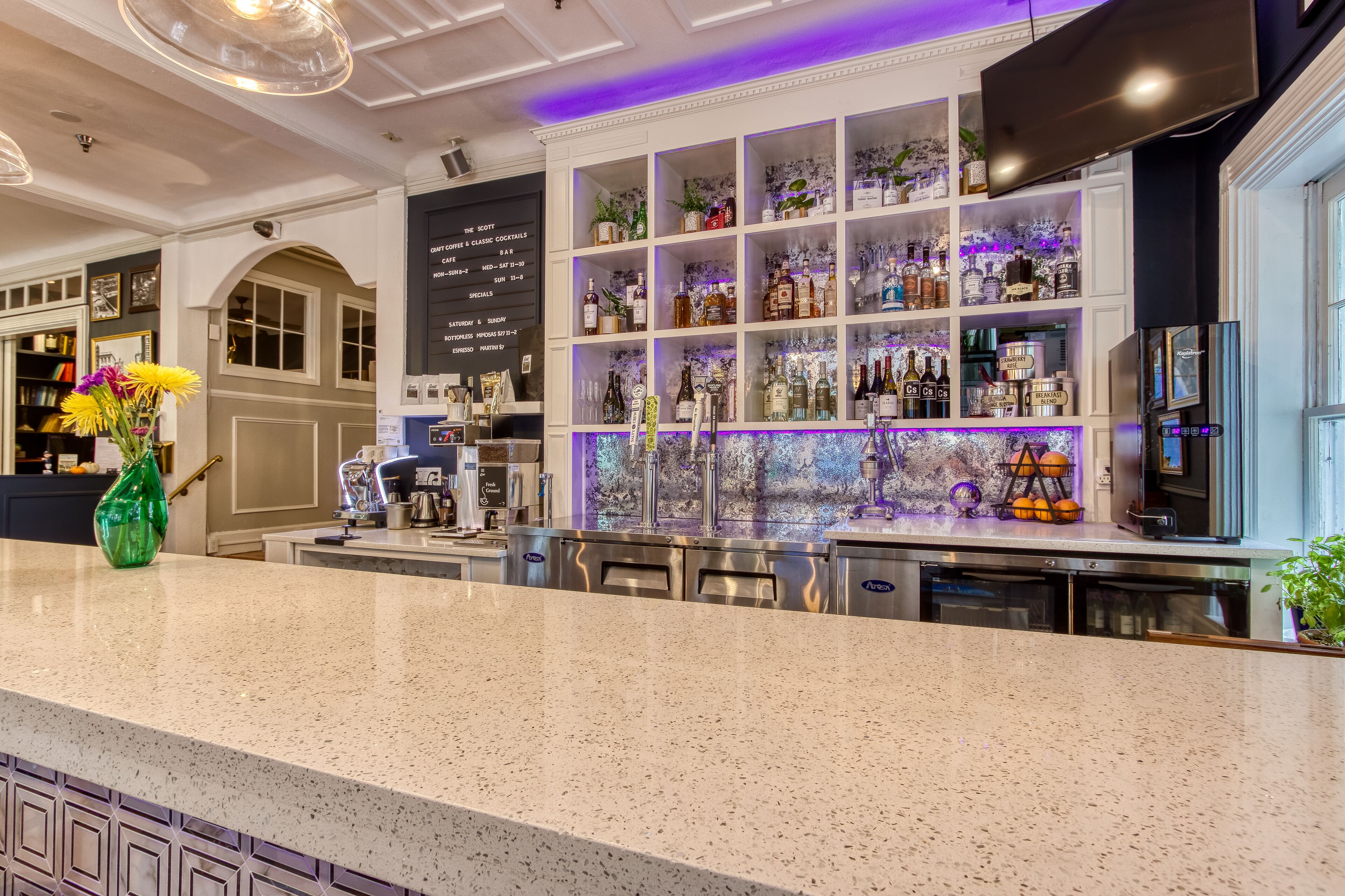 A bar area with shelves of liquor bottles, a coffee machine, and a decorative vase with flowers.