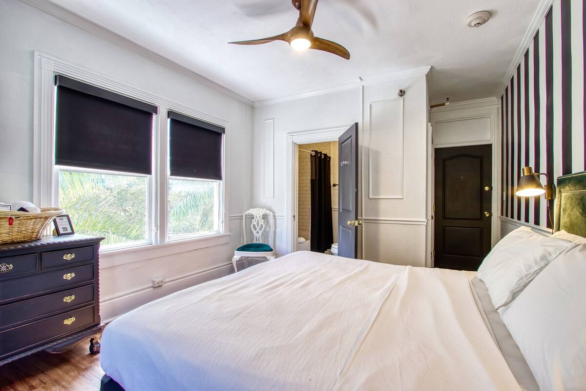 A bedroom with a bed, dresser, chair, and a ceiling fan.