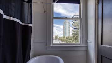 Een badkamer met een bad, een raam met uitzicht op hoge gebouwen en een deur.