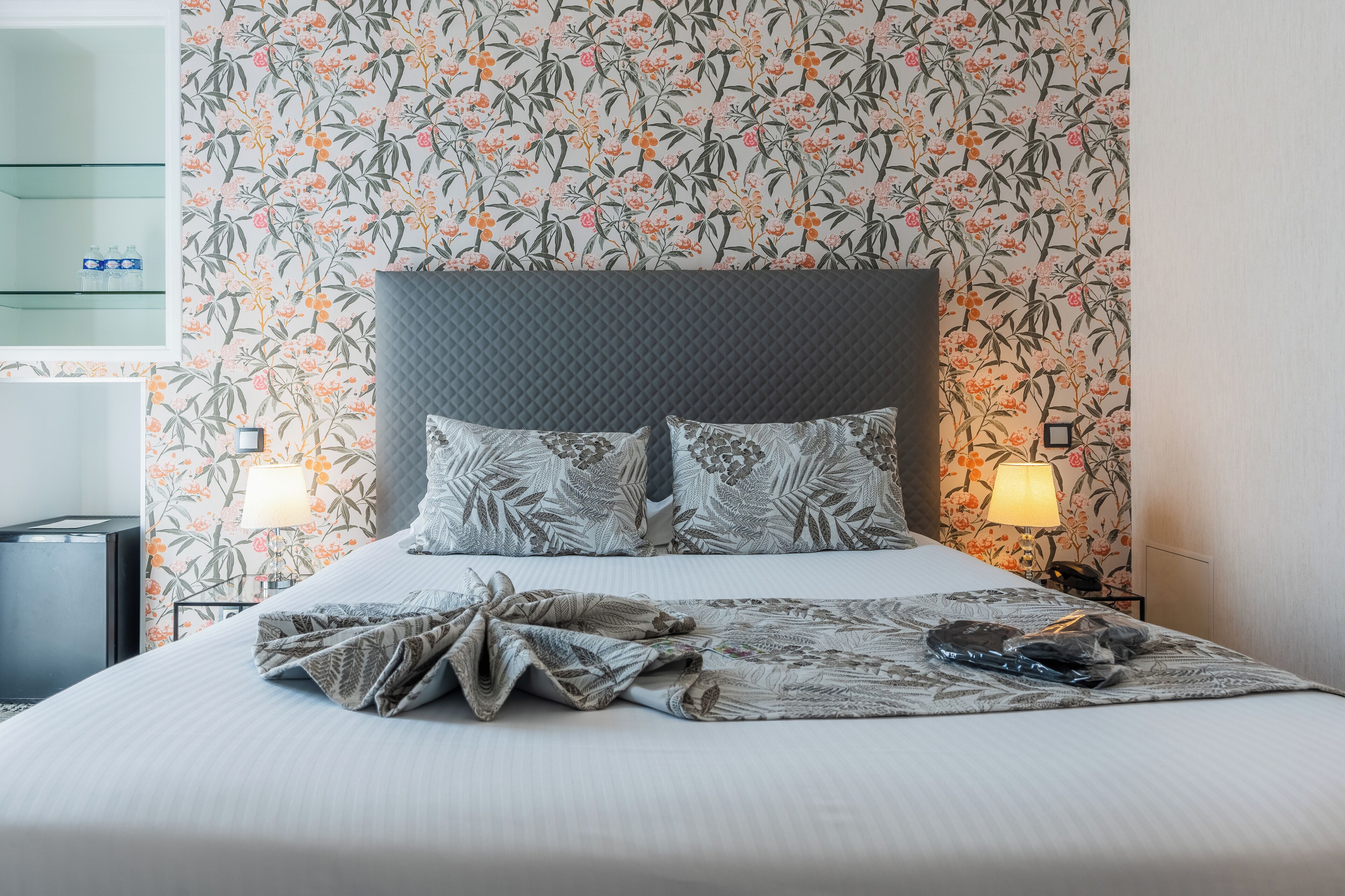 Una cama bien hecha con colcha estampada y almohadas, cabecera acolchada y dos lámparas de noche.