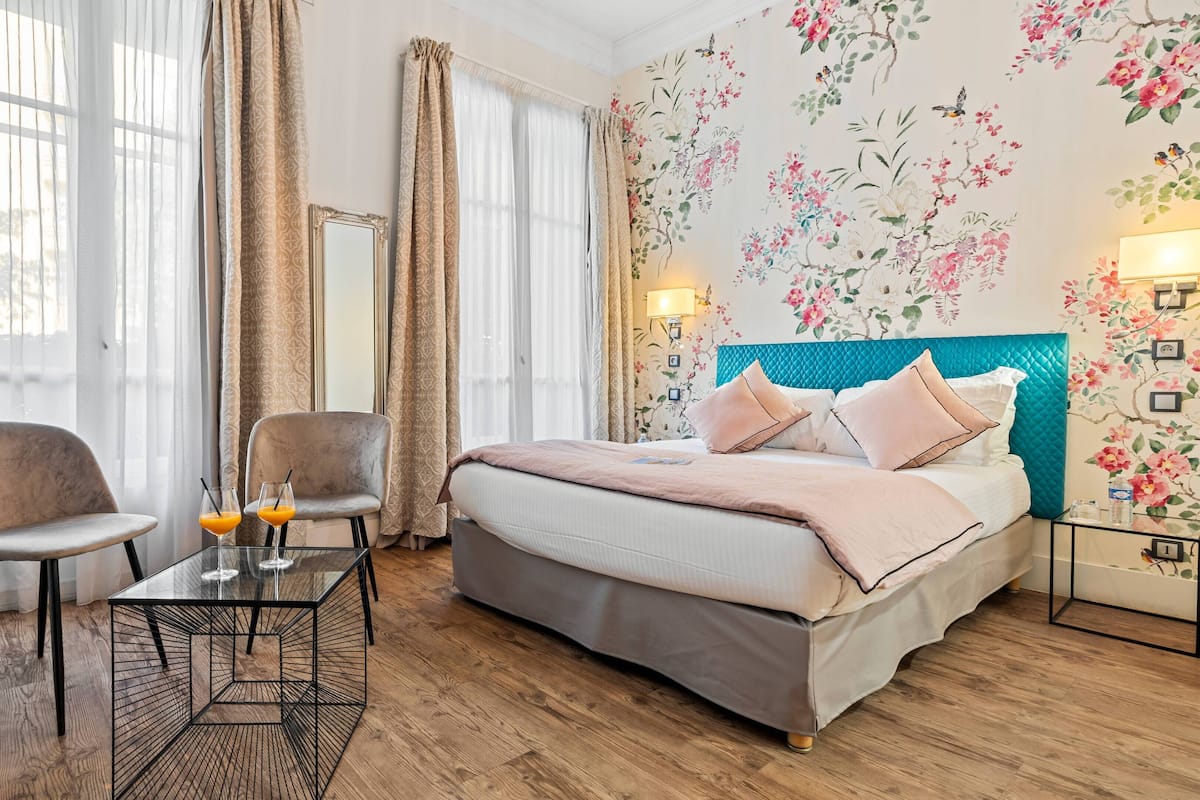 A hotel room with a bed, two armchairs, a glass coffee table, and a wooden floor.