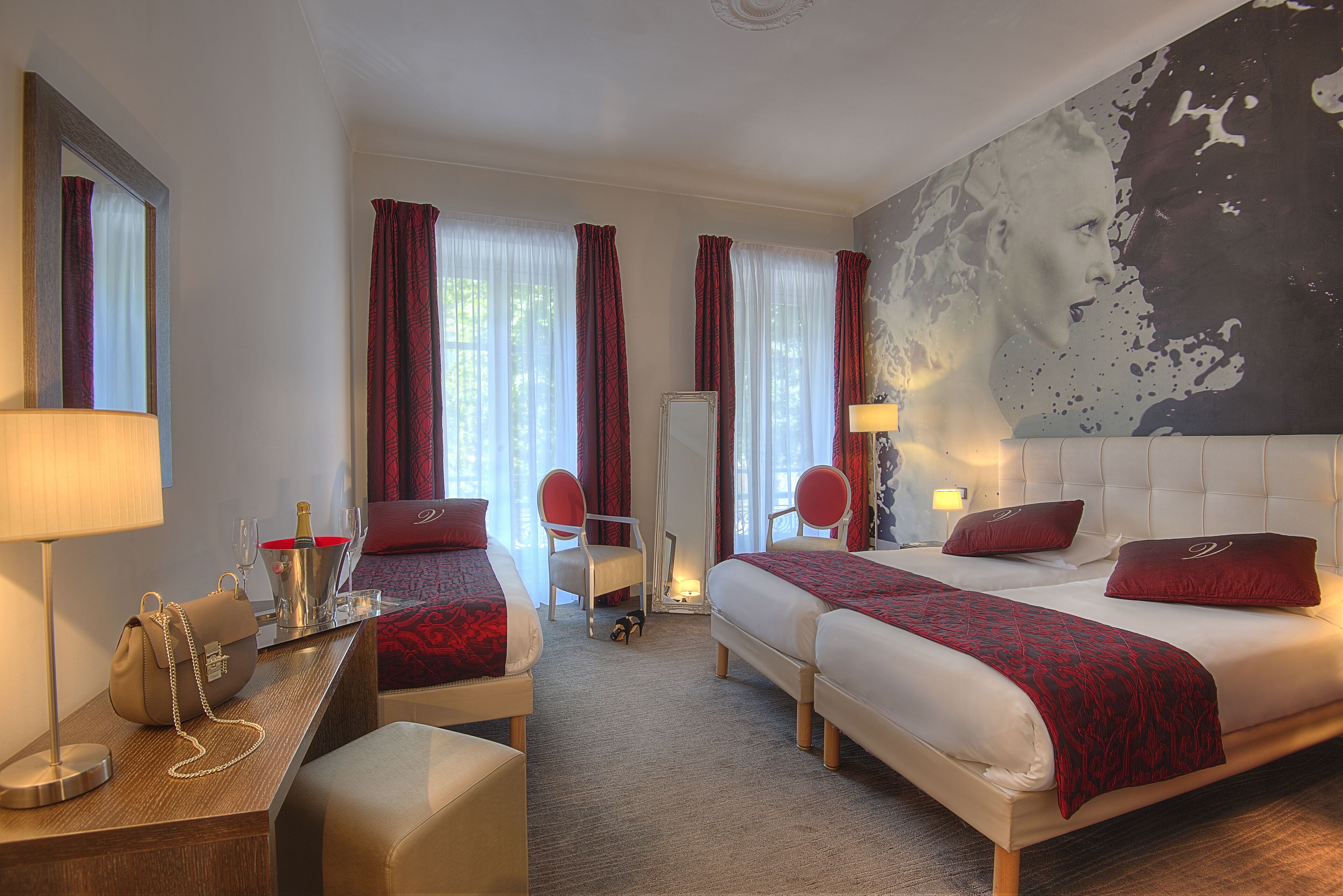 Une chambre d’hôtel avec deux lits, un bureau avec une lampe, une chaise, un minibar et un grand tableau abstrait accroché au mur.