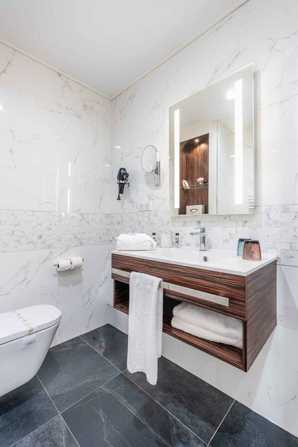 Un baño moderno con inodoro blanco, tocador de madera con espejo y suelo de baldosas negras.