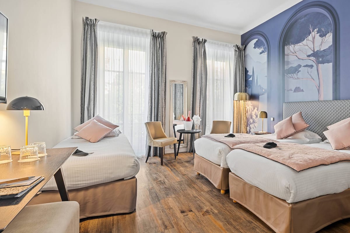 A hotel room with two beds, a desk, a chair, and a large mural on the wall.