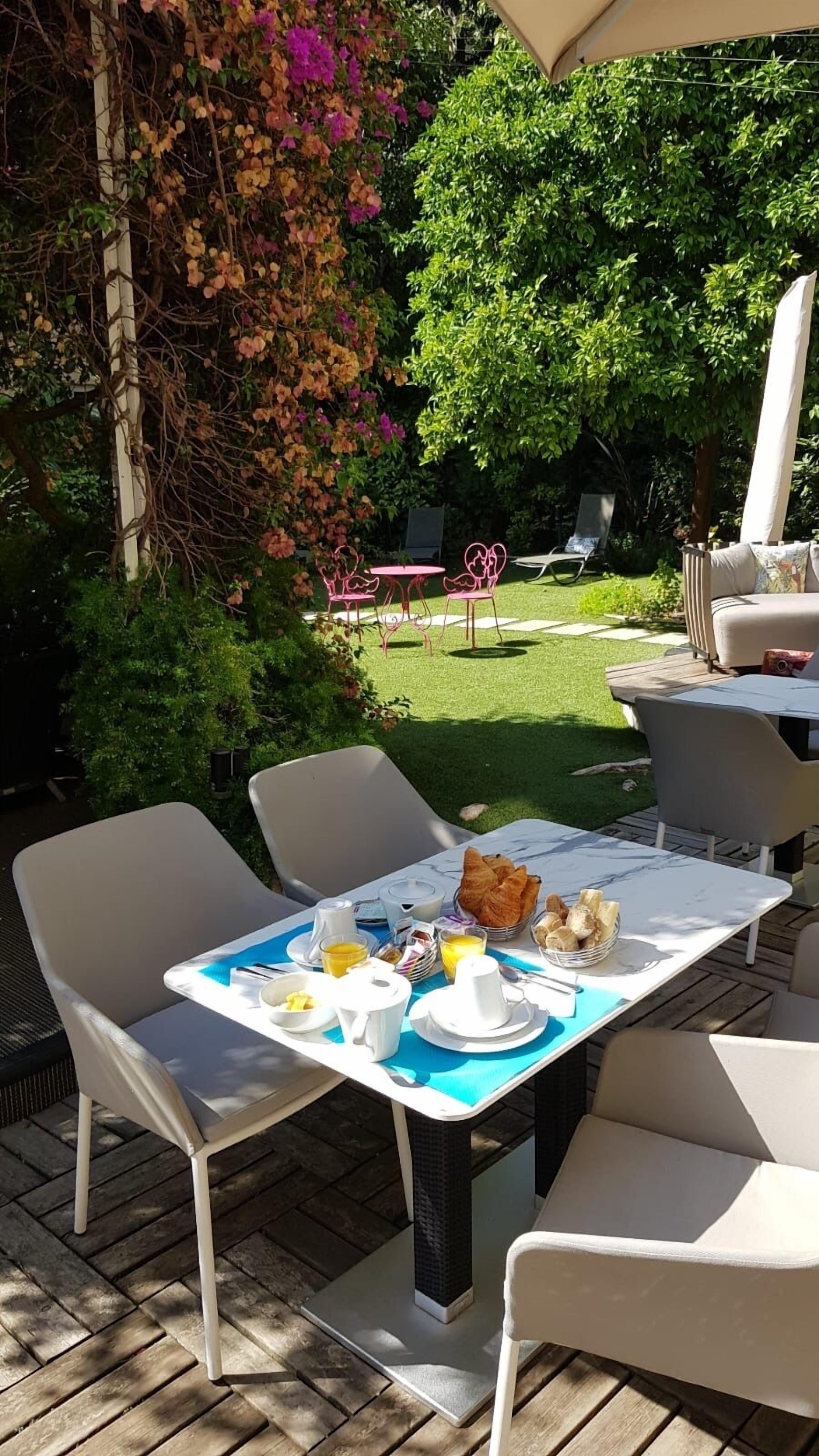 An outdoor dining area with a table set for breakfast, surrounded by chairs and a garden view.