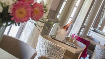 Un comedor con una mesa dispuesta para dos, con una silla de textura, un jarrón de flores y una botella de champán.