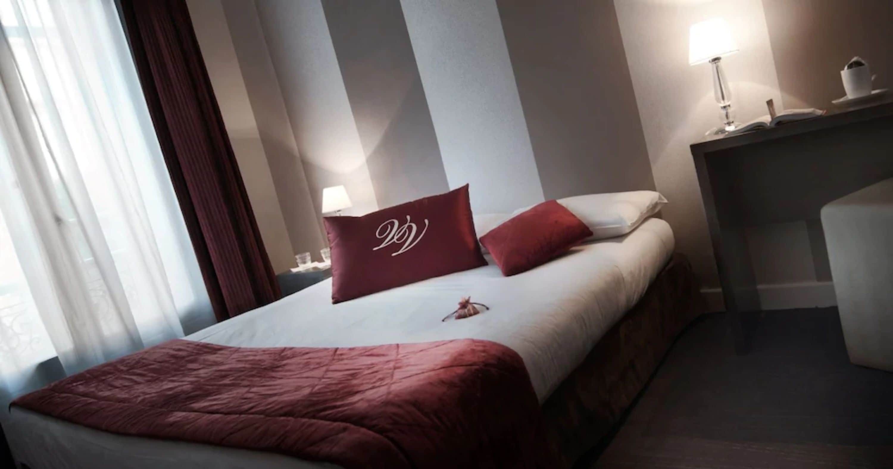A hotel room with a bed, a nightstand with a lamp, and a window with curtains.