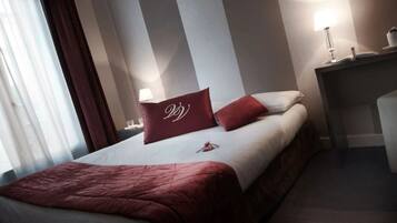 A hotel room with a bed, a nightstand with a lamp, and a window with curtains.