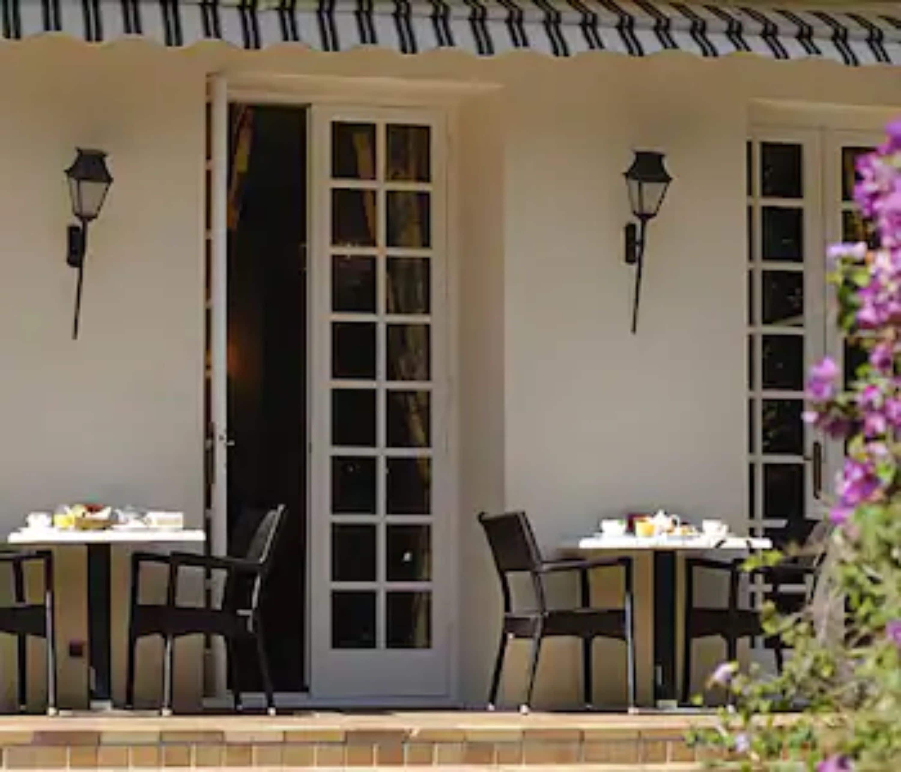 A patio area with two tables and chairs, a door, and two wall-mounted lamps.