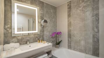 A modern bathroom with a large mirror, a white sink, a bathtub, and a potted orchid.