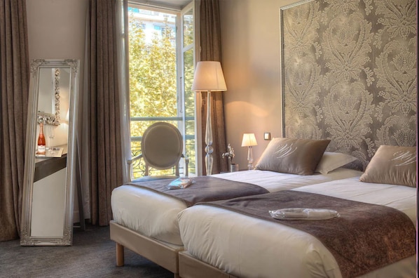 A hotel room with a large bed, two bedside tables, a mirror, a window with curtains, and a patterned wall. - Villa Victoria (Nice)