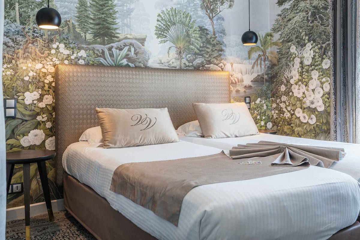 A bedroom with a large bed, two pillows with monogrammed initials, a headboard with a textured design, and a mural of a forest scene on the wall.